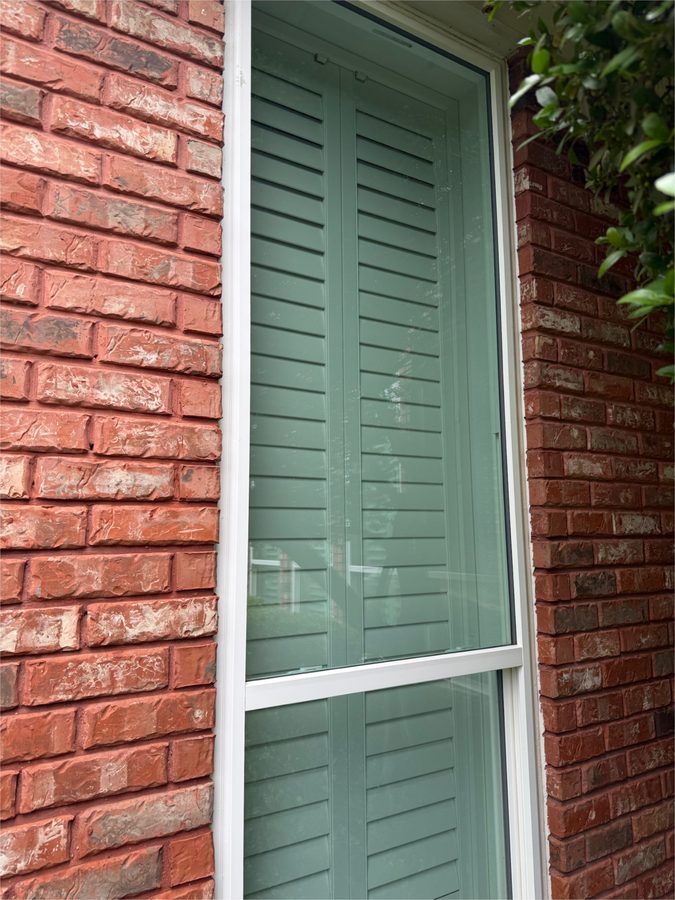Clean window beside red brick with green shutters