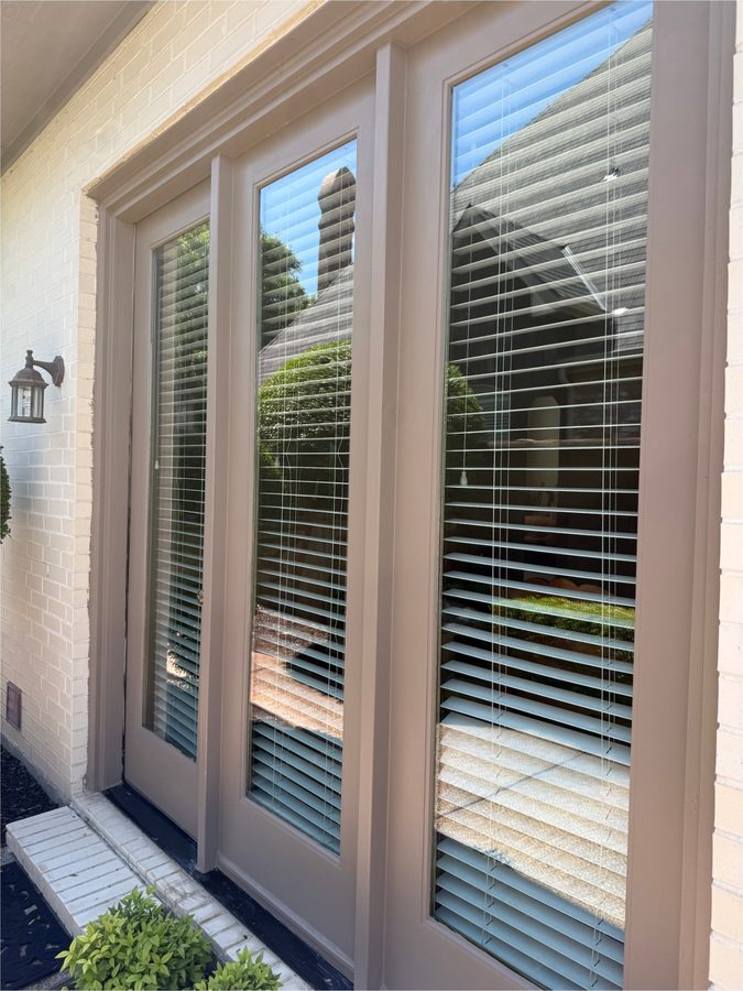 Floor-to-ceiling glass patio doors with brown trim on a white brick wall