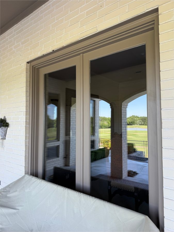 Clean glass panels on a white brick home reflecting a covered patio